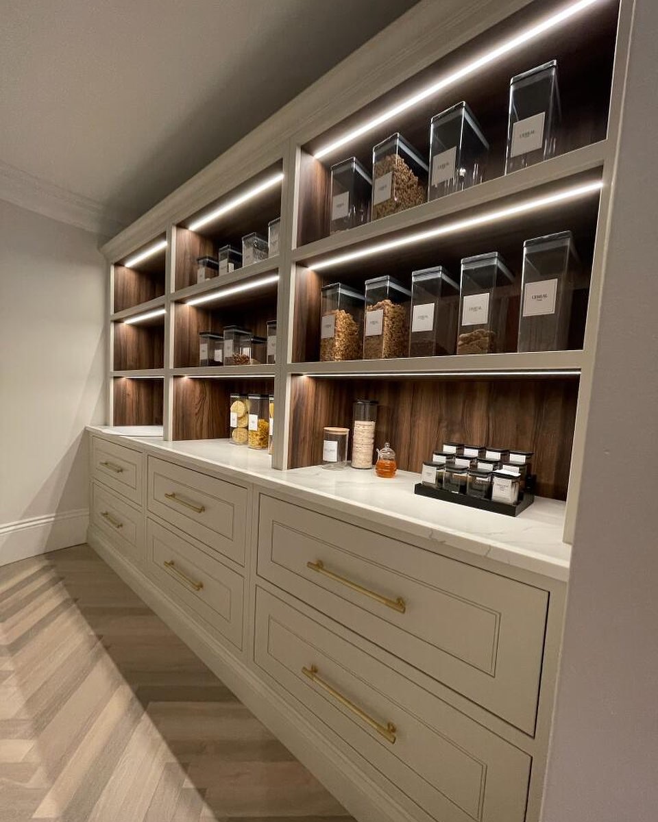 Luxury built-in pantry with walnut backing, brass hardware, LED shelf lighting, and marble countertop on Long Island's North Shore